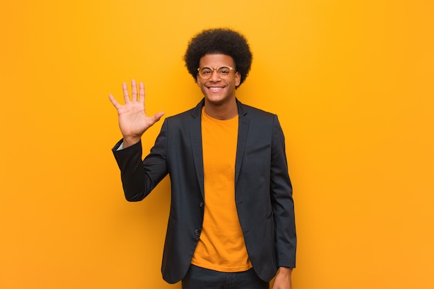 Joven hombre afroamericano de negocios sobre una pared naranja que muestra el número cinco