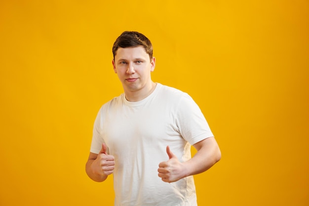 Joven hombre apuesto con camiseta blanca sobre fondo amarillo aprobando hacer un gesto positivo con los pulgares hacia arriba sonriendo y feliz por el éxito Gesto de ganador