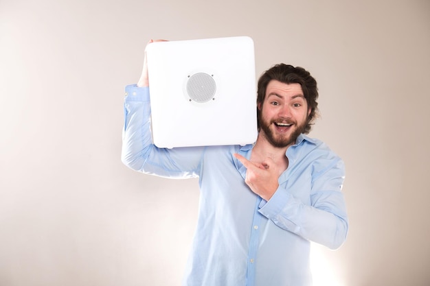 Foto joven hombre atractivo sosteniendo un altavoz bluetooth portátil blanco en el hombro sobre un fondo gris