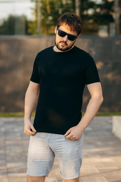 Foto joven hombre barbudo con estilo en una camiseta negra y gafas de sol foto de la calle