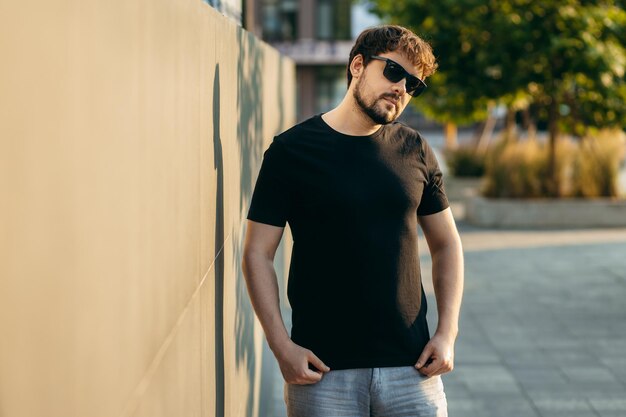 Joven hombre barbudo con estilo en una camiseta negra y gafas de sol Foto de la calle