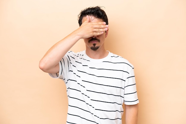 Joven hombre caucásico aislado en fondo beige cubriendo los ojos con las manos no quiere ver algo