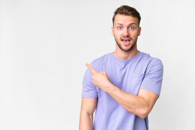Joven hombre caucásico guapo sobre fondo blanco aislado sorprendido y señalando lado