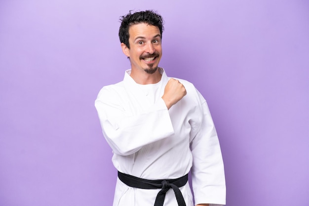 Joven hombre caucásico haciendo karate aislado en fondo púrpura celebrando una victoria