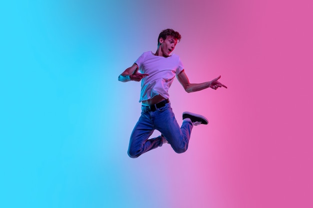 Joven hombre caucásico saltando alto sobre fondo de estudio azul-rosa degradado en luz de neón