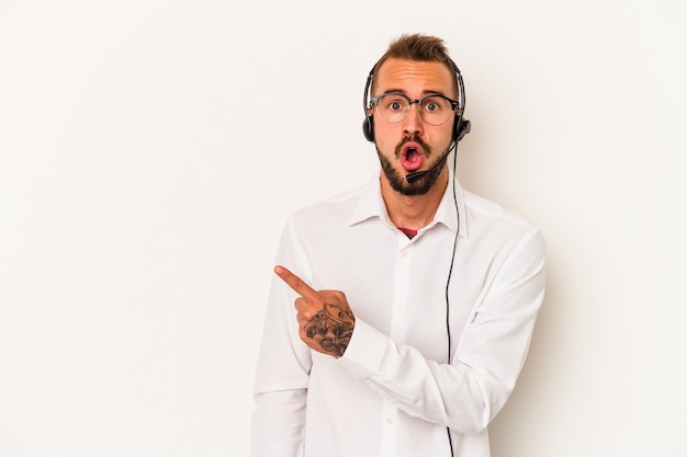 Joven hombre caucásico telemarketer con tatuajes aislado sobre fondo blanco apuntando hacia el lado