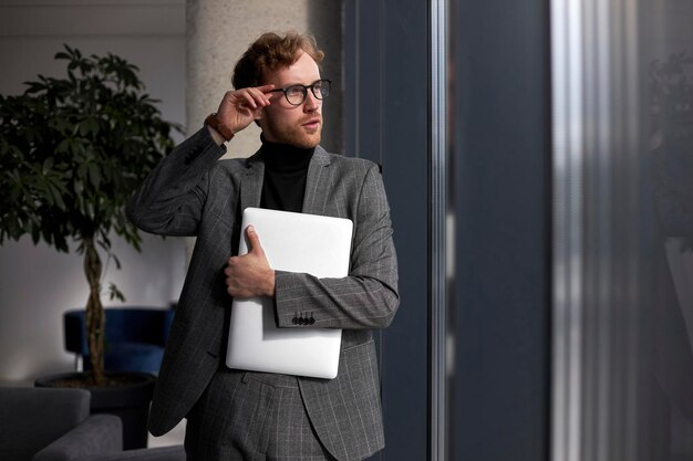 Joven hombre de confianza hipster con traje elegante, anteojos correctos con laptop