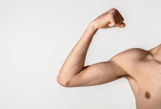 Joven hombre delgado brazo en un fondo gris hombre débil músculo flexionante hombre flaco va en para los deportes construye