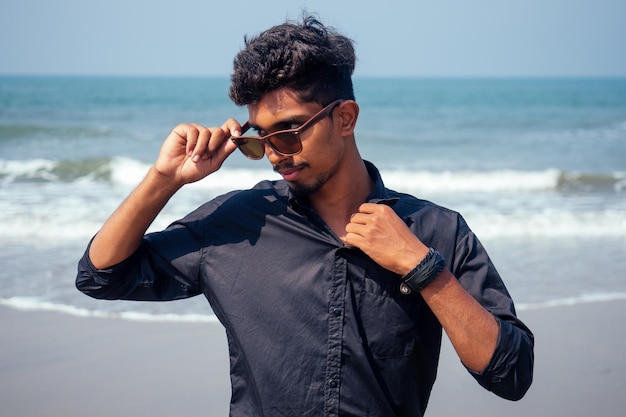 Joven hombre elegante hindú posando con gafas de sol vacaciones activas en la playa en la feliz playa de Goa India semmertime. concepto de protección solar spf.