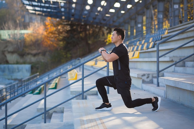 Joven hombre en forma asiático activo dedicado al ejercicio físico que se extiende por la calle al aire libre. Atleta masculino en entrenamiento de ropa deportiva estadio urbano de la ciudad Estilo de vida saludable Deportes fitness fuera Calentamiento antes de trotar