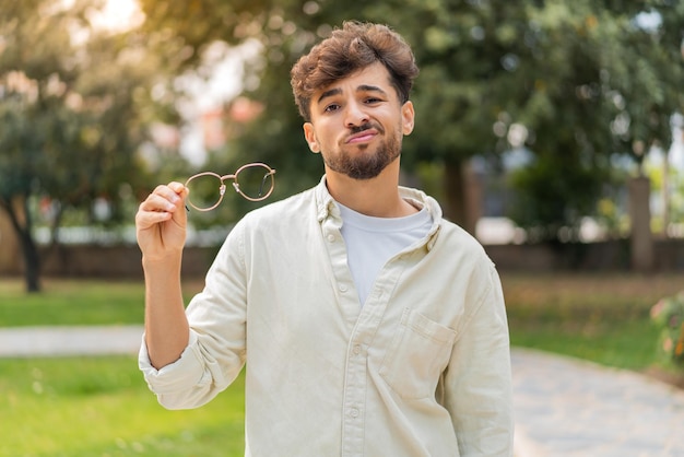 Foto joven hombre guapo árabe con gafas al aire libre con expresión triste