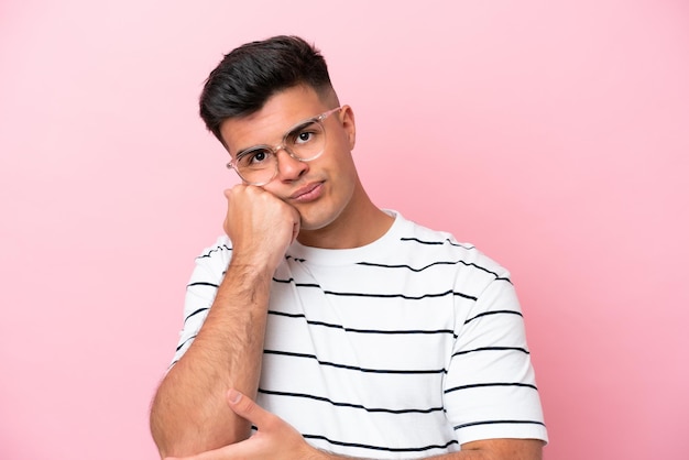 Joven hombre guapo caucásico aislado sobre fondo rosa con gafas y con expresión triste