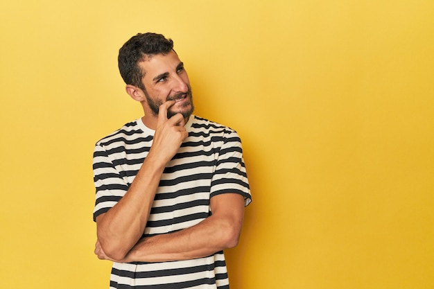 Foto joven hombre hispano con fondo amarillo relajado pensando en algo mirando un espacio de copia