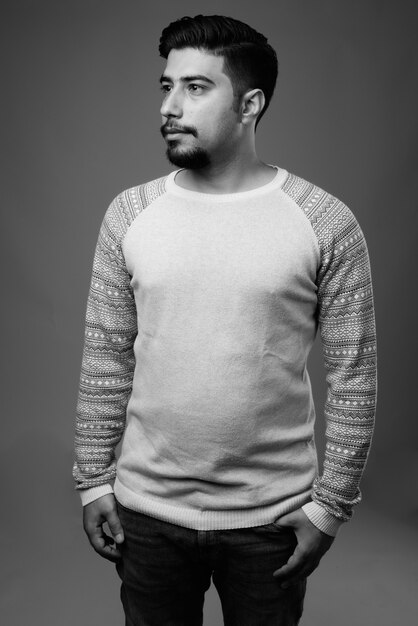 Joven hombre iraní barbudo con ropa casual contra la pared gris en blanco y negro
