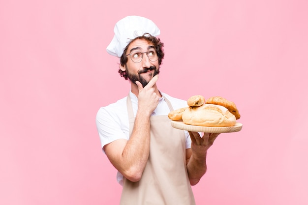 Joven hombre loco panadero sosteniendo pan contra la pared rosa