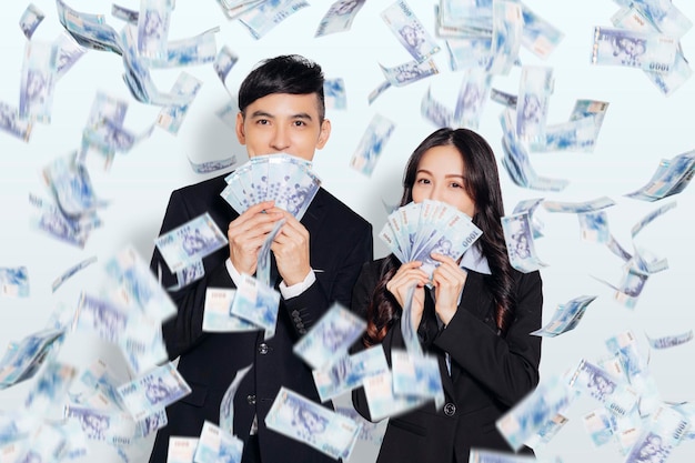 Joven hombre y mujer de negocios mostrando el dinero bajo la lluvia de dinero