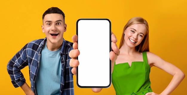 Foto joven hombre y mujer positivos demostrando un gran teléfono inteligente en blanco en la cámara