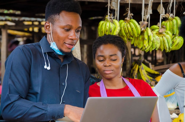 El joven hombre de negocios africano se siente emocionado mientras le muestra a una mujer del mercado información en su computadora portátil.