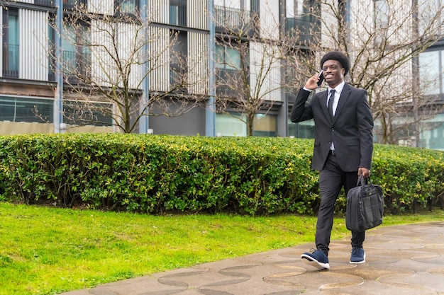 Joven hombre de negocios africano viajando mientras habla con el móvil al aire libre