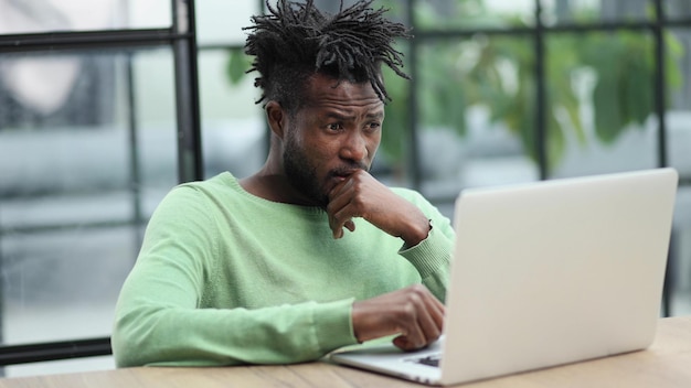 Joven hombre de negocios afroamericano sentado en una oficina de loft o en un café trabajando en una nueva puesta en marcha en línea