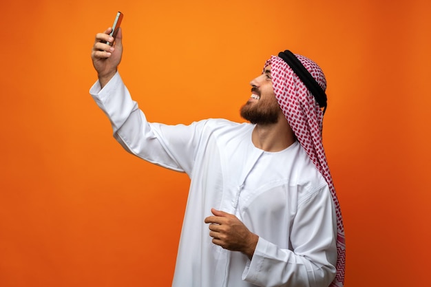 Joven hombre de negocios árabe usando un teléfono inteligente con fondo naranja