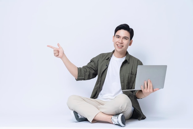 Joven hombre de negocios asiático sentado y usando una computadora portátil en el fondo