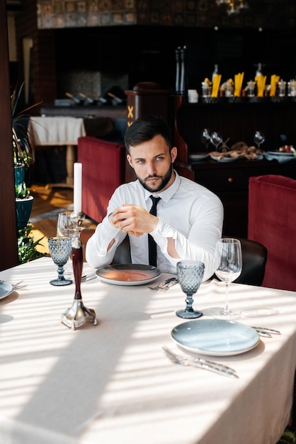 Un joven hombre de negocios barbudo está sentado en una mesa en un restaurante elegante y esperando su pedido Servicio al cliente en el catering