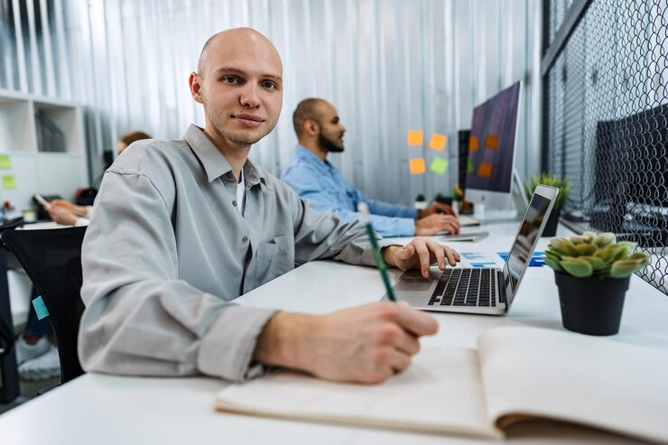 Foto joven hombre de negocios calvo sentado en el escritorio en la oficina trabajando en la computadora