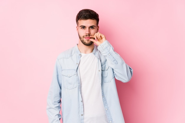 Joven hombre de negocios caucásico posando en una pared blanca aislada con los dedos en los labios manteniendo un secreto. <Mixto>