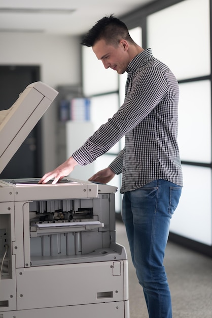 Foto un joven hombre de negocios copia documentos en una fotocopiadora en el moderno interior de la oficina de inicio, ropa informal