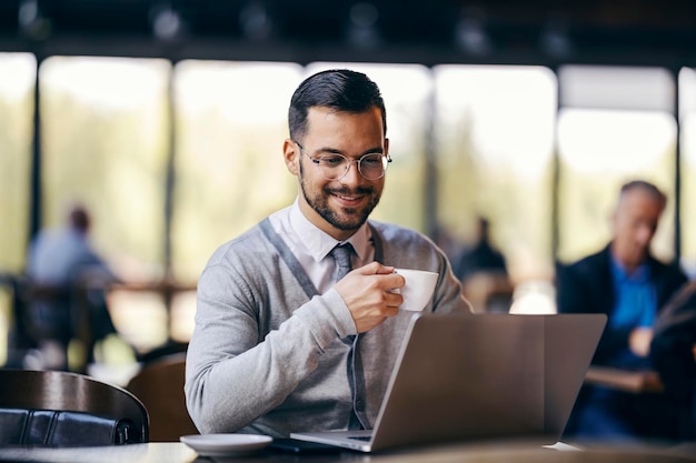 Un joven hombre de negocios está sentado en una cafetería tomando café y trabajando de forma remota en una computadora portátil