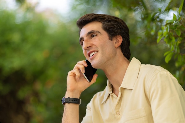 Un joven hombre de negocios exitoso tiene una conversación telefónica mientras descansa al aire libre