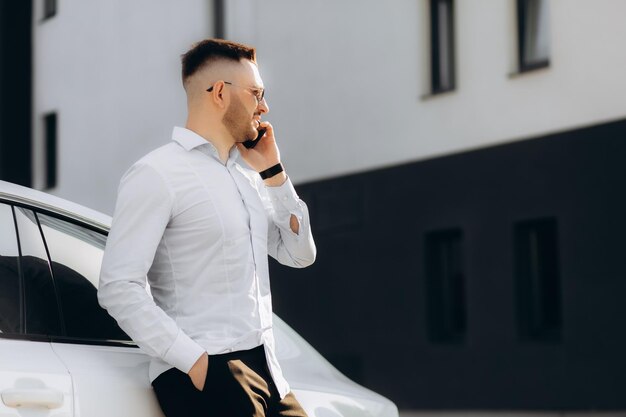 Joven hombre de negocios feliz con carpeta caminando y hablando por teléfono celular cerca del centro de negocios