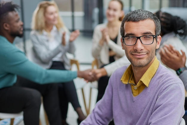 Foto un joven hombre de negocios feliz con un suéter morado se sienta en el contexto de sus colegas