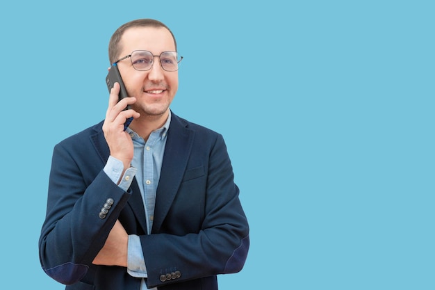 Foto joven hombre de negocios hablando en un teléfono inteligente con un fondo azul en el estudio