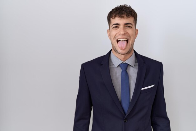 Foto joven hombre de negocios hispano con traje y corbata sacando la lengua feliz con el concepto de emoción de expresión divertida