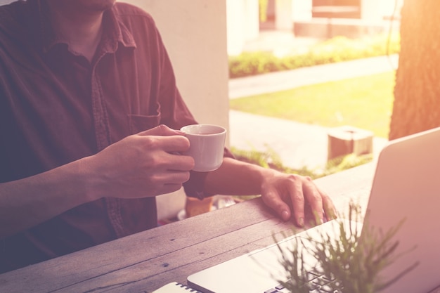 joven hombre de negocios mano sosteniendo taza de café y el uso de equipo portátil en la cafetería con vintage entonado.