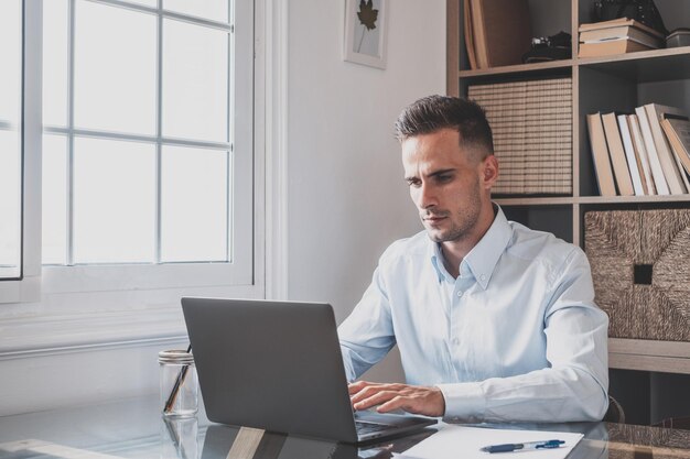 Joven hombre de negocios millennial caucásico feliz trabajando en casa en el escritorio con computadora portátil o computadora divirtiéndose Joven hombre en videoconferencia cuidando del negocio o mercado