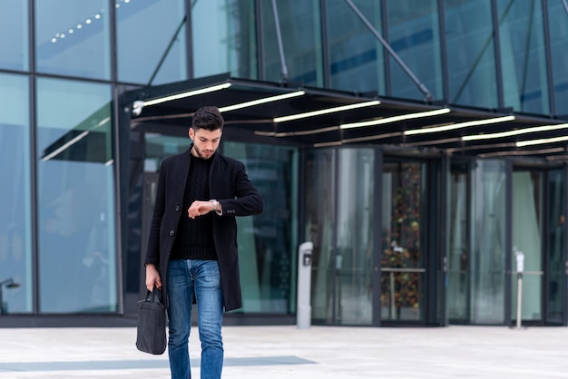 Joven hombre de negocios mirando su reloj empresario masculino y comerciante revisando el tiempo moderno rascacielos financiero en el fondo nuevo espacio de copia de negocios financieros