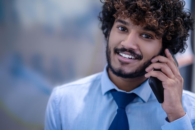 Un joven hombre de negocios de pelo rizado con una camisa azul hablando por teléfono