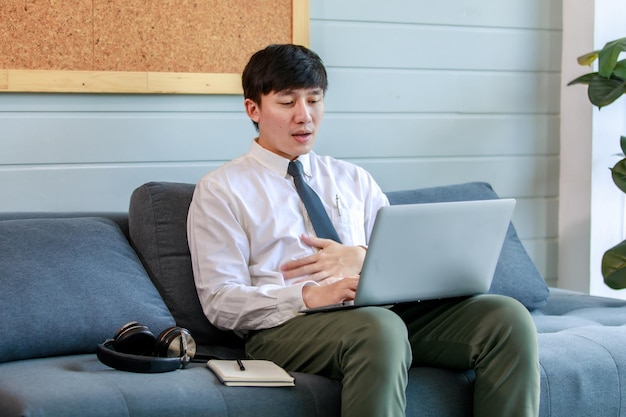 Joven hombre de negocios que trabaja con un auricular portátil y una nota de papel en el sofá de descanso del vestíbulo de la oficina y cierra los ojos para pensar en una solución sobre la estrategia de marketing y la red de planificación para resolver una tarea difícil