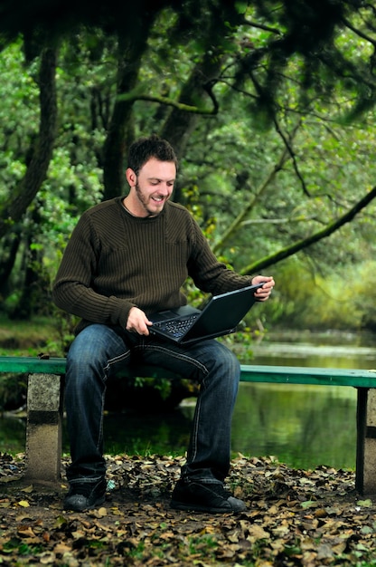 un joven hombre de negocios que trabaja en una laptop al aire libre con naturaleza verde en segundo plano