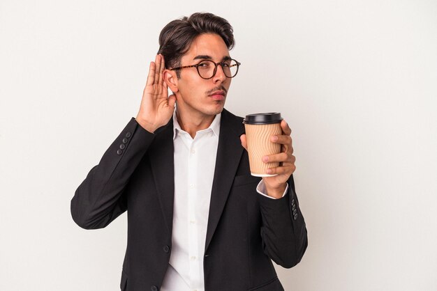 Joven hombre de negocios de raza mixta sosteniendo café para llevar aislado en fondo blanco tratando de escuchar un chisme.