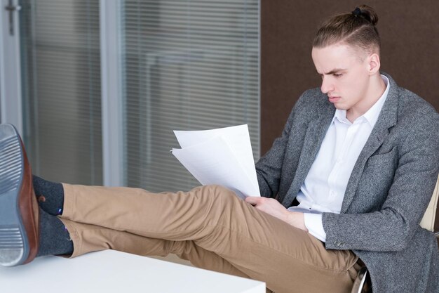 Joven hombre de negocios relajado leyendo documentos en la oficina Gerente exitoso confiado centrado en papeles