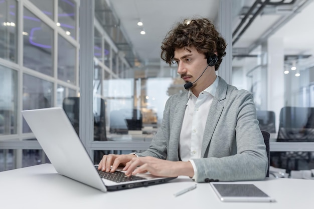 Un joven hombre de negocios serio con auriculares está sentado en la oficina en un escritorio y se está concentrando