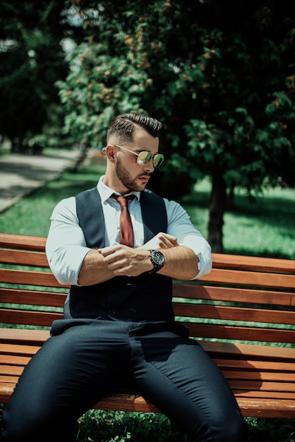 Un joven hombre de negocios sexy con traje sentado en el parque en un descanso laboral