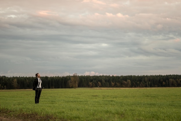 Joven hombre de negocios con traje elegante en un prado verde bajo un cielo nublado de otoño.