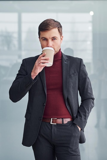 Un joven hombre de negocios con traje de lujo y ropa con taza de está en el interior de la oficina. | Foto Premium