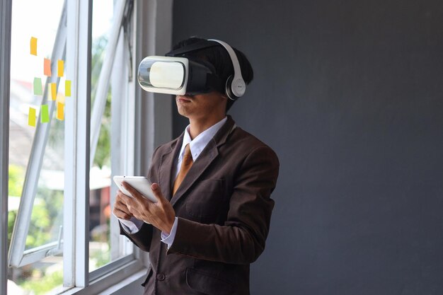 Joven hombre de negocios usando gafas VR y sosteniendo un teléfono inteligente en la oficina.