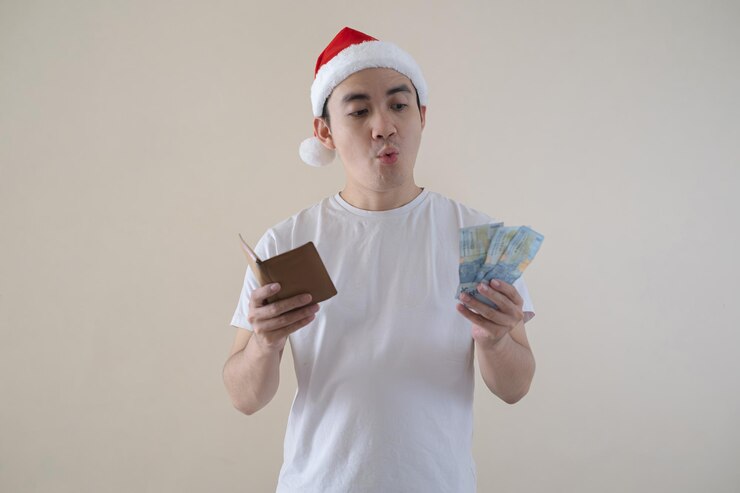 Joven hombre de Papá Noel asiático sosteniendo una billetera y dinero con una venta de invierno de choque en un fondo aislado